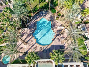Vista aérea de un resort con una gran piscina rodeada de palmeras y zonas de descanso.