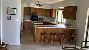 A modern kitchen with wooden cabinets, a central island with stools, and a dining area with a wooden table and chairs.