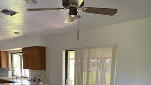 A dining area with a wooden table and green chairs, a kitchen with wooden cabinets, and a ceiling fan.