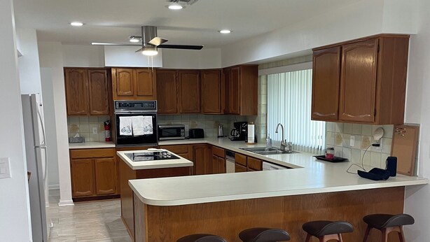 A modern kitchen with wooden cabinets, a central island with stools, a microwave, oven, and a ceiling fan.