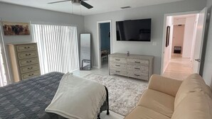 A bedroom with a bed, a sofa, a TV, a dresser, and a ceiling fan.