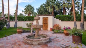 A courtyard with a stone fountain, palm trees, and potted plants. - Maison du Soleil (Palm Springs)