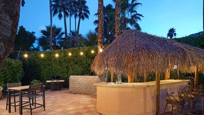 An outdoor patio with a thatched-roof bar area, seating, and a grill. - Maison du Soleil (Palm Springs)