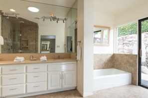 A modern bathroom with a large mirror, a bathtub, and a vanity with multiple drawers. - Maison du Soleil (Palm Springs)