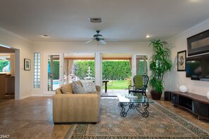 A spacious living room with a beige sofa, a glass coffee table, and a large potted plant. - Maison du Soleil (Palm Springs)