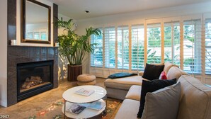 A living room with a fireplace, a large mirror, a sofa, a coffee table, and a potted plant. - Maison du Soleil (Palm Springs)