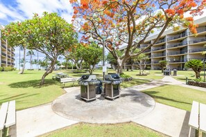 Relax and socialize in our outdoor area, featuring a barbecue station, picnic tables, and benches amidst lush greenery and vibrant trees.