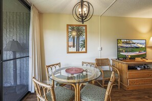 Cozy living space with a dining table and four chairs, a TV, and a picture of palm trees on the wall.