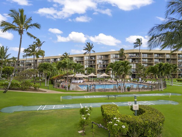 A hotel with a swimming pool surrounded by palm trees and a golf course.