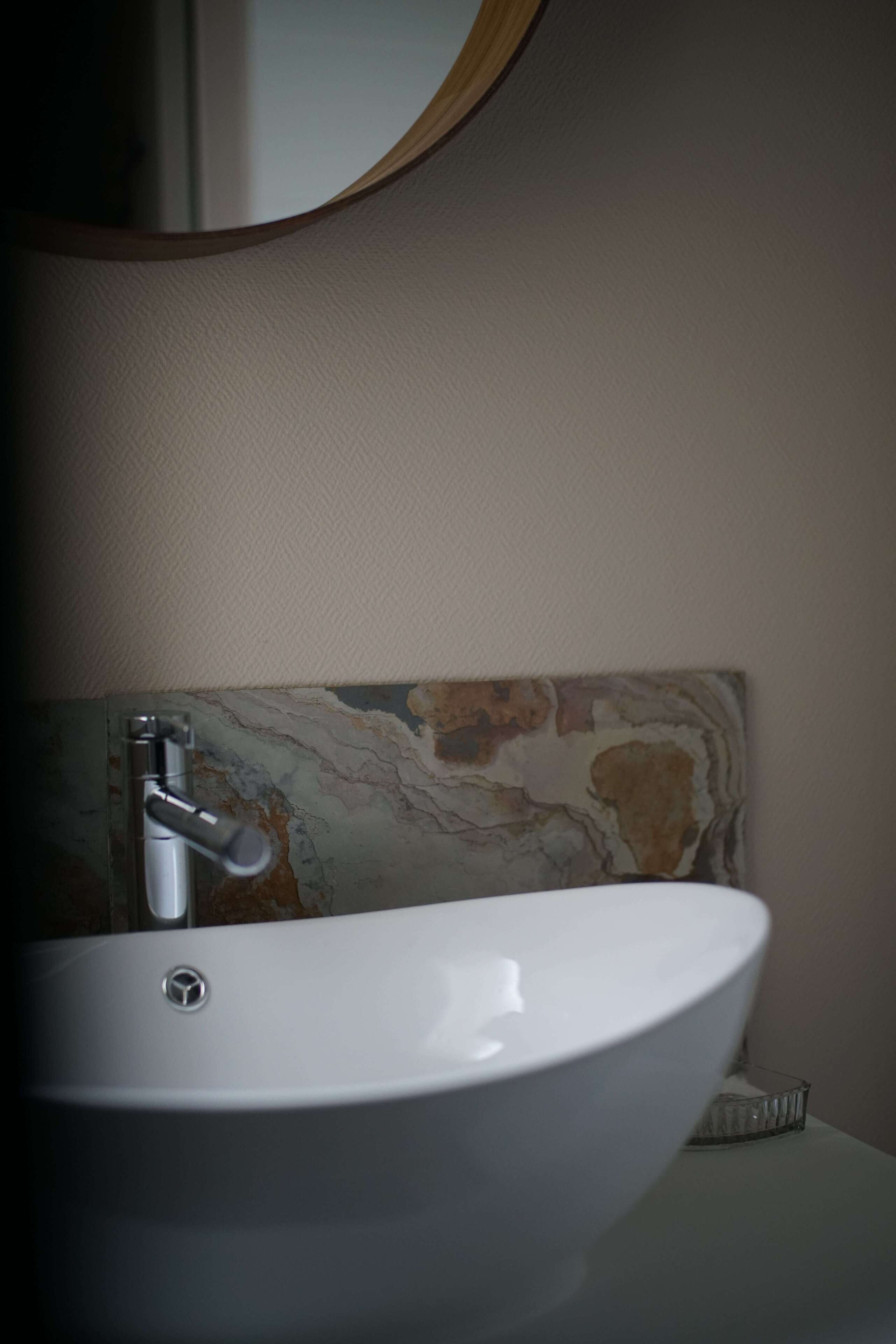 A bathroom with a white sink, a modern faucet, and a textured wall behind the sink.