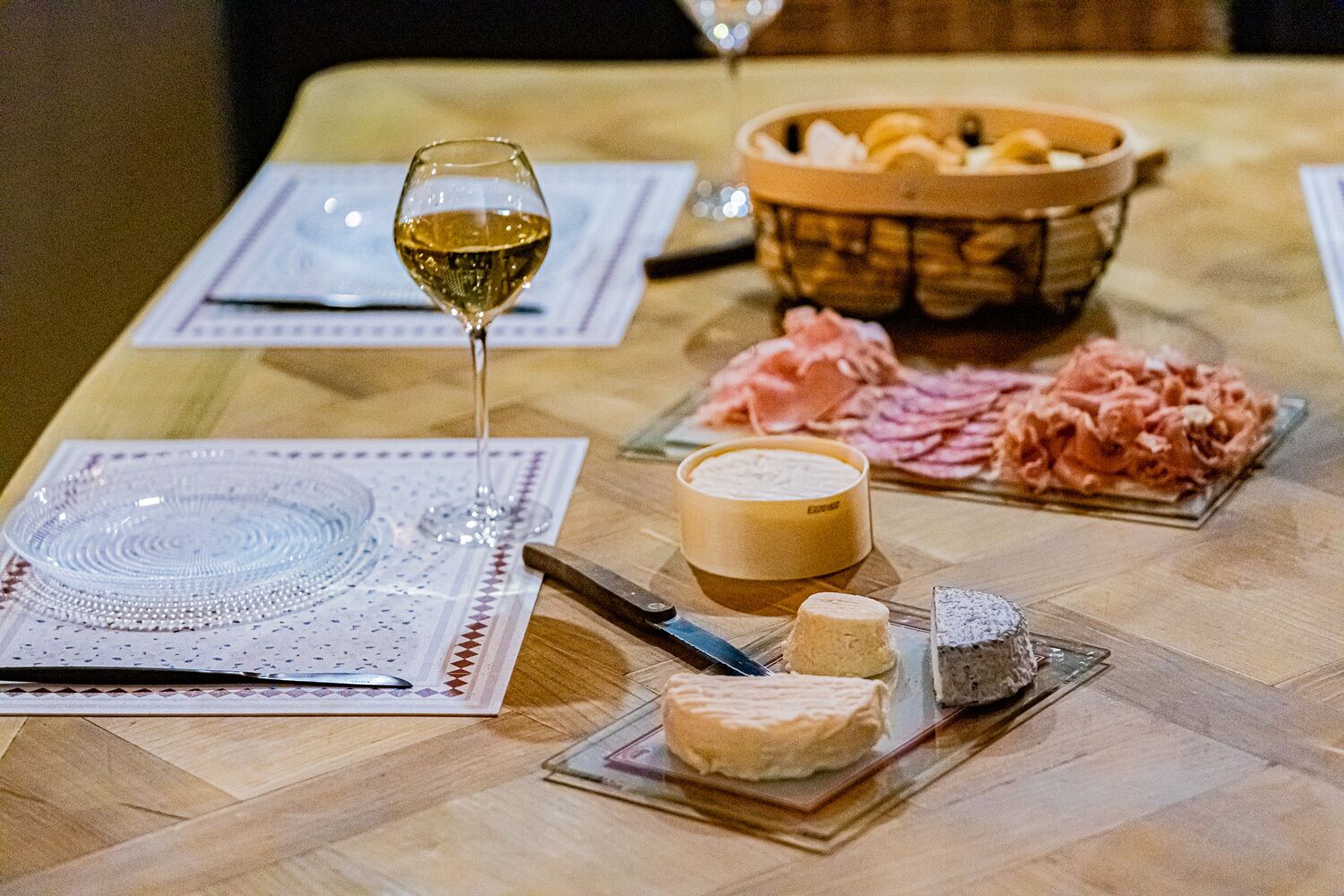 Een tafel met een glas witte wijn, een kaasplank en verschillende kazen.