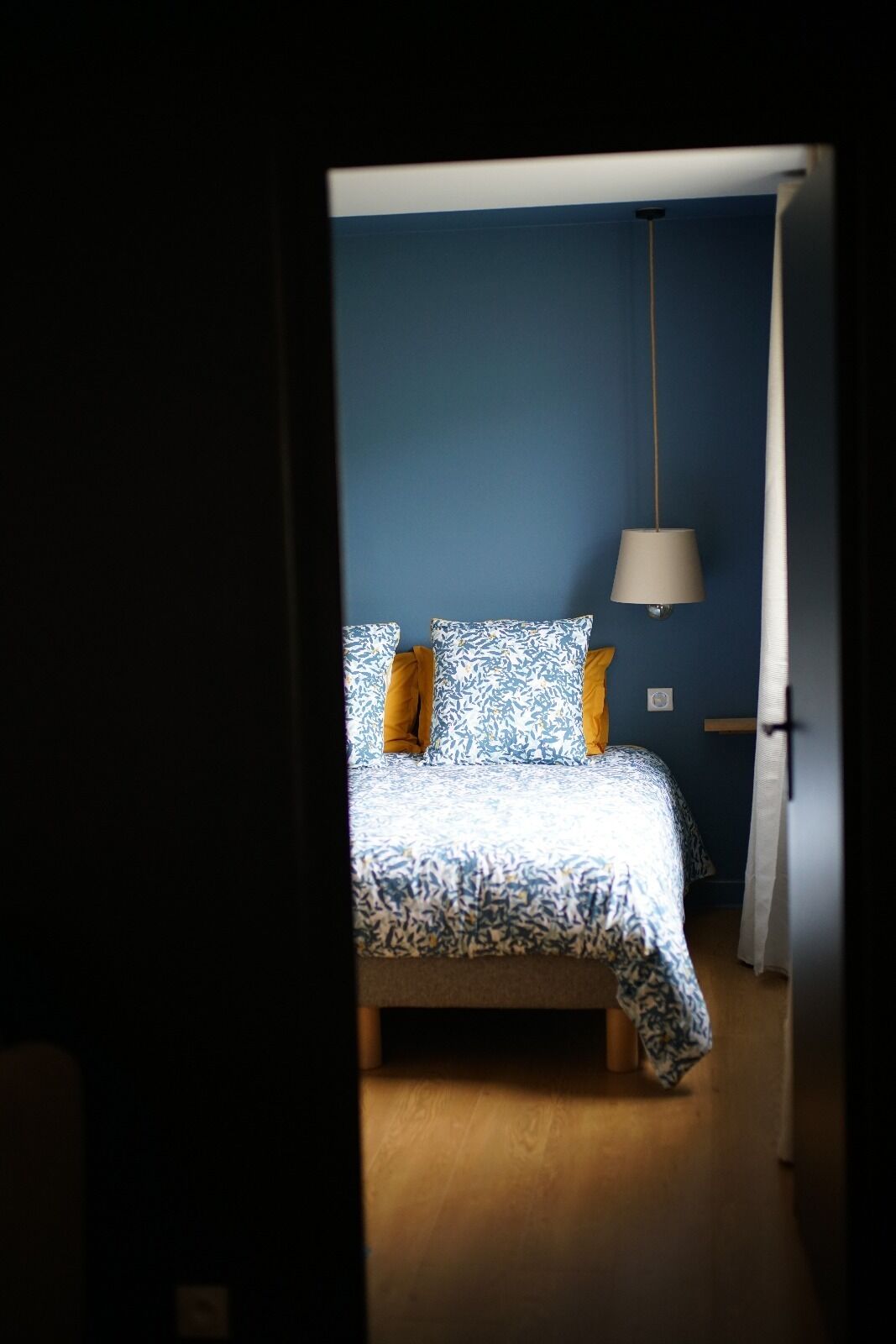 Et soveværelse med en seng, en lampe og et gardin.