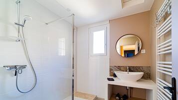 Een moderne badkamer met een douche met glazen wand, een witte wastafel en een spiegel erboven.