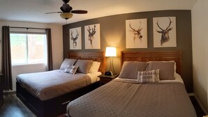 A hotel room with two beds, a ceiling fan, and wall art of deer heads.