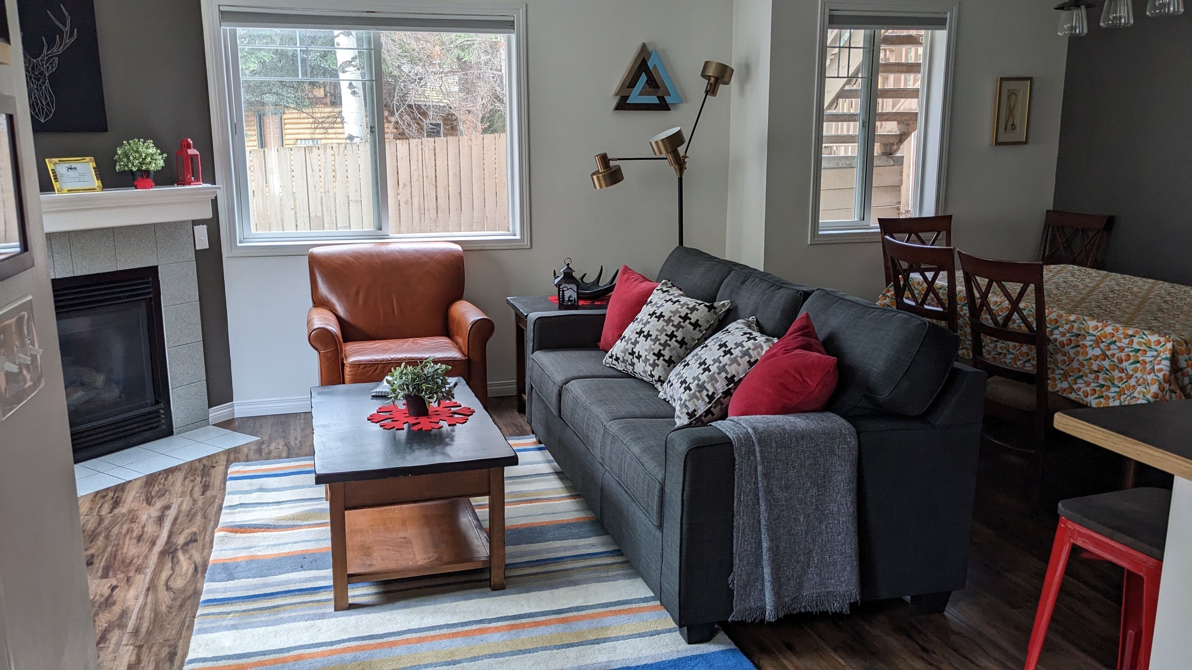 A cozy living room with a fireplace, a leather armchair, a grey sofa with patterned cushions, and a striped rug.