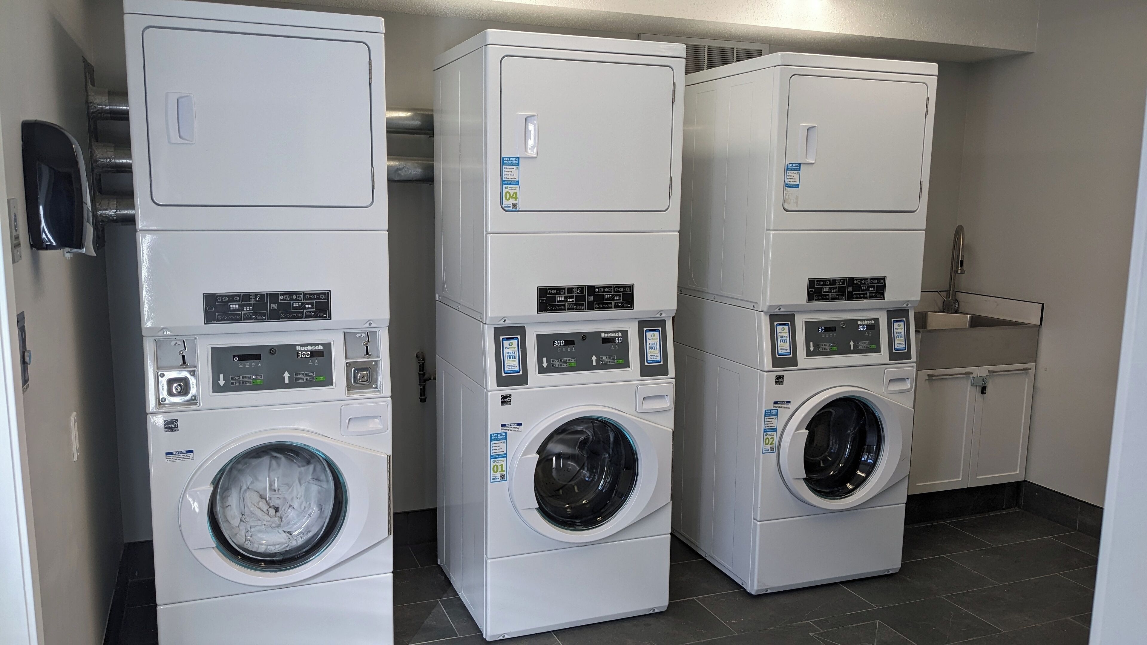 A laundry facility with three stacked washing machines, a sink, and a tiled floor.