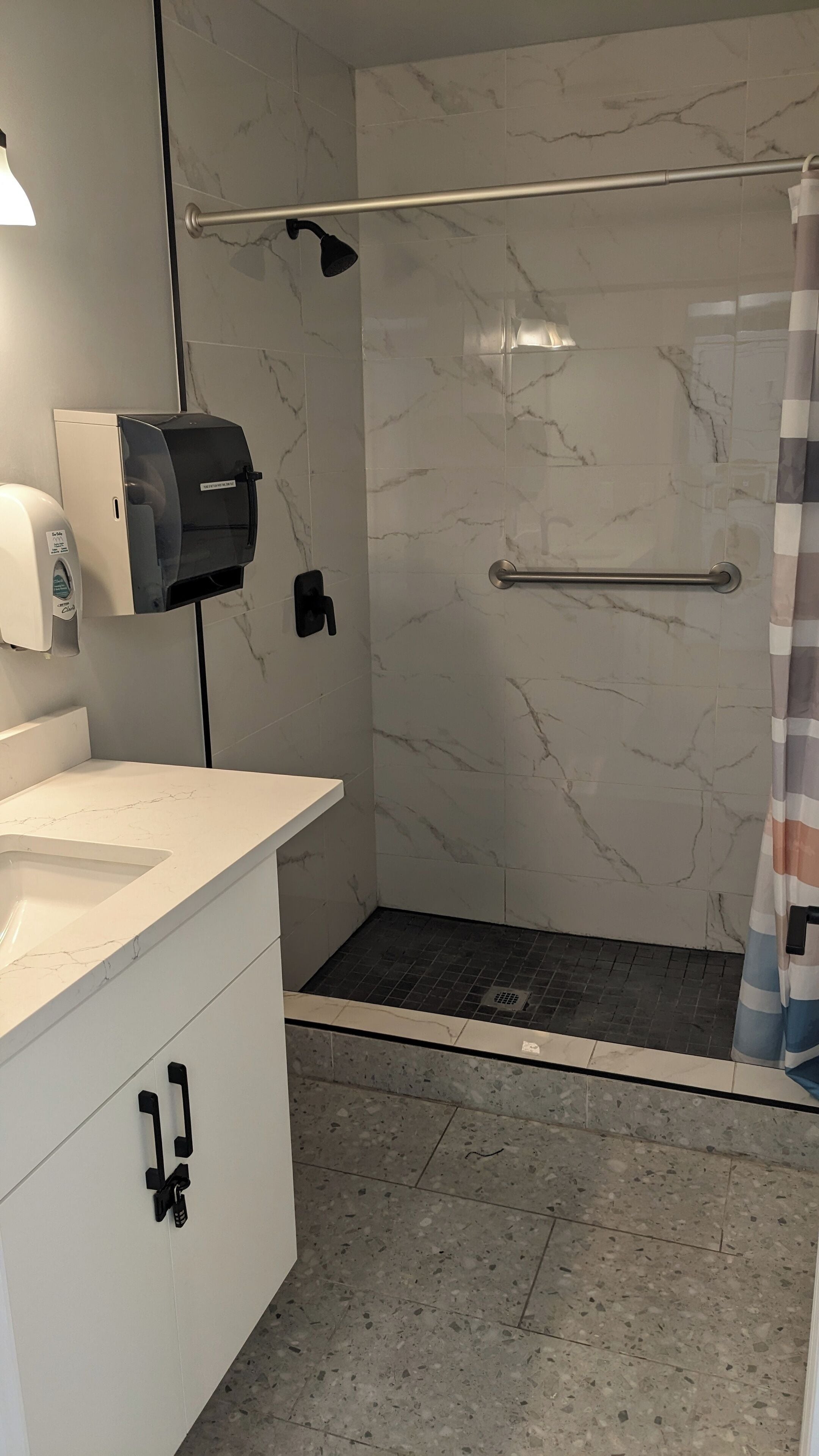 Ein modernes Badezimmer mit einer Marmerdusche, einem weißen Waschbecken und einem Handtuchspender.