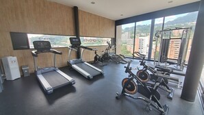 A modern gym with treadmills, stationary bikes, and weight machines, large windows with a city view. - ★18th Floor★Coolest building in Medellin★RoofTop Pool/Jacuzzi/Gym★Amazing Views★ (Medellin)