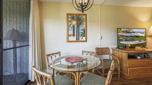 A dining area with a glass table, wicker chairs, a television, and a framed picture on the wall.