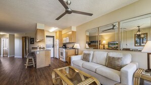A modern living room with a sofa, a glass coffee table, and a kitchen area with wooden cabinets and a microwave.