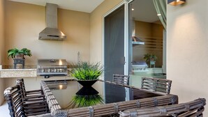 Un espacio al aire libre para comer con una parrilla, sillas de mimbre y plantas en macetas.
