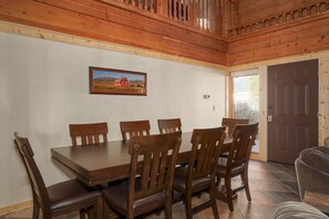 Een eethoek met een houten tafel en stoelen, een ingelijst beeld aan de muur en een deur op de achtergrond.