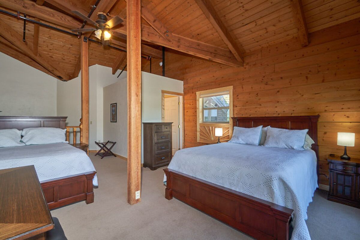 Une chambre dans une cabane en bois, avec deux lits, un ventilateur de plafond et une fenêtre.