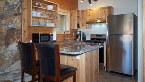 Eine Küche mit Holzausstattung, einer Arbeitsplatte aus Granit, einem Edelstahlkühlschrank und einer Steinwand.