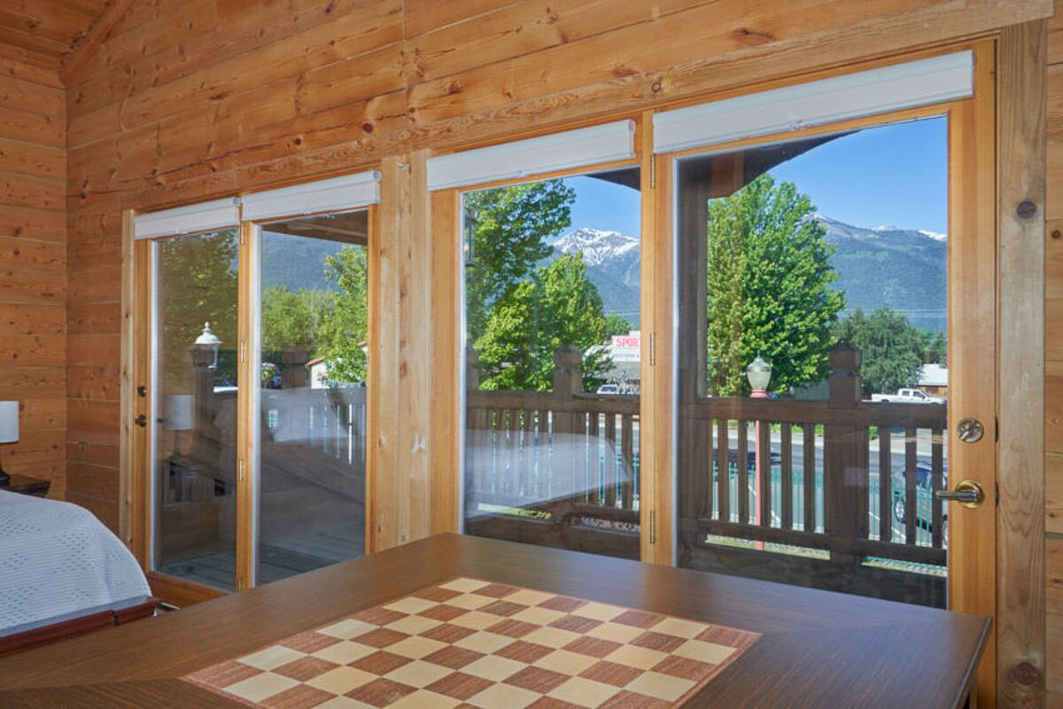 Une cabane en bois avec une grande table à carreaux et une vue sur la montagne, visible à travers des portes vitrées.