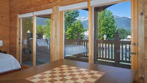 Eine Holzhütte mit einem großen karierten Tisch und Blick auf einen Berg durch Glastüren.