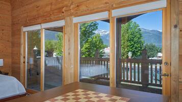 Une cabane en bois avec une grande table à carreaux et une vue sur la montagne, visible à travers des portes vitrées.