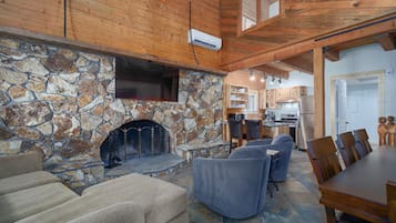 Un salon chaleureux avec une cheminée en pierre, un plafond en bois et un coin repas comprenant une table et des chaises en bois.
