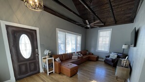 Een ruime woonkamer met een grote hoekbank, een houten vloer en een plafondventilator.