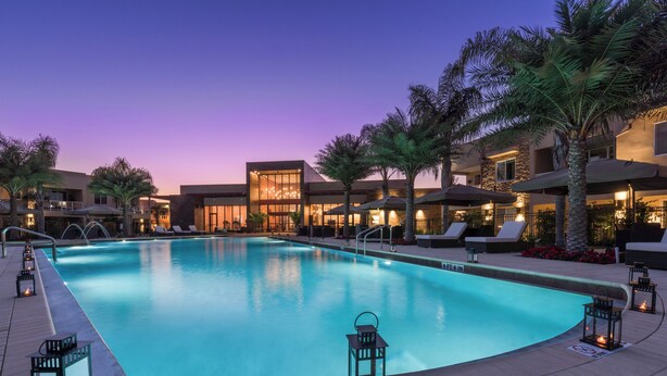 A swimming pool with lounge chairs and umbrellas, surrounded by palm trees and a building with a stone facade. - Just 3.5m to Disney/Lovely Home/No Resort fee/Parking/Wi-Fi/Free Club House Use (Kissimmee)