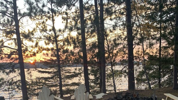 A wooden deck with Adirondack chairs and a fire pit in a forested area. - Lake House 100 yards off snowmobile trail #8.  (Michigamme)