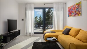 A modern living room with a sofa, a TV, and a view to the outside. - Villa Calypso with Pool (Podstrana)