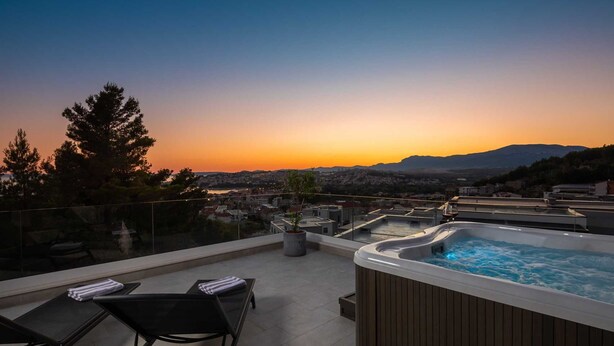 A rooftop terrace with a hot tub, seating area, and a view of a cityscape at sunset. - Villa Calypso with Pool (Podstrana)
