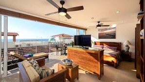 A spacious balcony with a view of the sea, a bedroom with a bed, a TV, and a ceiling fan. - DREAM CONDO: OCEAN VIEWS & ONLY STEPS FROM THE BEACH (Puerto Vallarta)