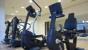 A row of stationary bikes in a gym with a wooden floor and a large mirror reflecting the equipment and a window in the background. - DREAM CONDO: OCEAN VIEWS & ONLY STEPS FROM THE BEACH (Puerto Vallarta)