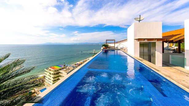 A modern infinity pool with a clear view of the sea and a building with a satellite dish. - DREAM CONDO: OCEAN VIEWS & ONLY STEPS FROM THE BEACH (Puerto Vallarta)