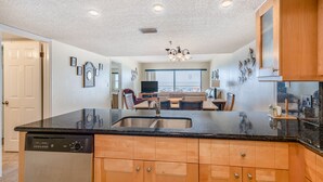 A kitchen with a dishwasher, wooden cabinets, a black countertop, and a chandelier.