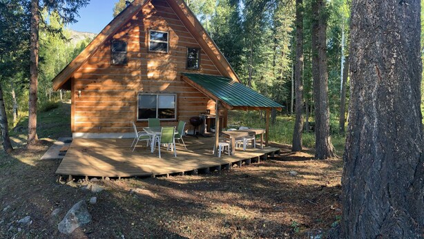 A wooden cabin with a deck, outdoor seating, and a green roof. - Cozy Cabin in the national forest  (Pagosa Springs)