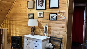A cozy room with wooden walls, a white dresser, a black heater, and framed pictures on the wall. - Cozy Cabin in the national forest  (Pagosa Springs)