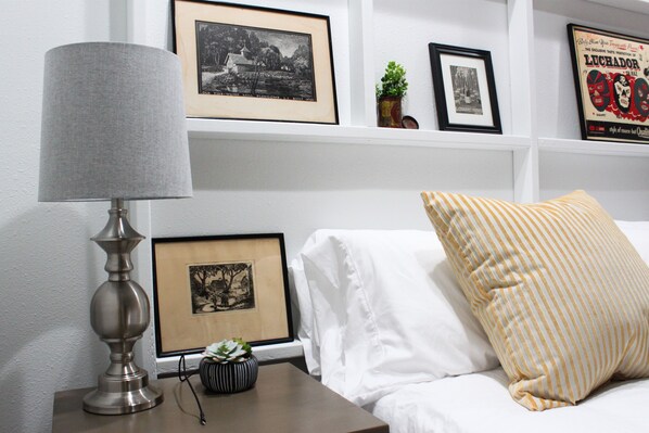 A neatly arranged bedroom with a bed, a bedside table with a lamp, and framed pictures on the wall.
