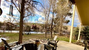 A covered patio with Adirondack chairs, a fire pit, and a view of a river and buildings in the background.