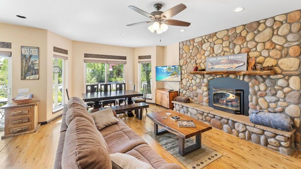 A spacious living room with a stone fireplace, a ceiling fan, and a large TV.