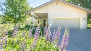A single-story house with a garage, surrounded by a garden with purple flowers.