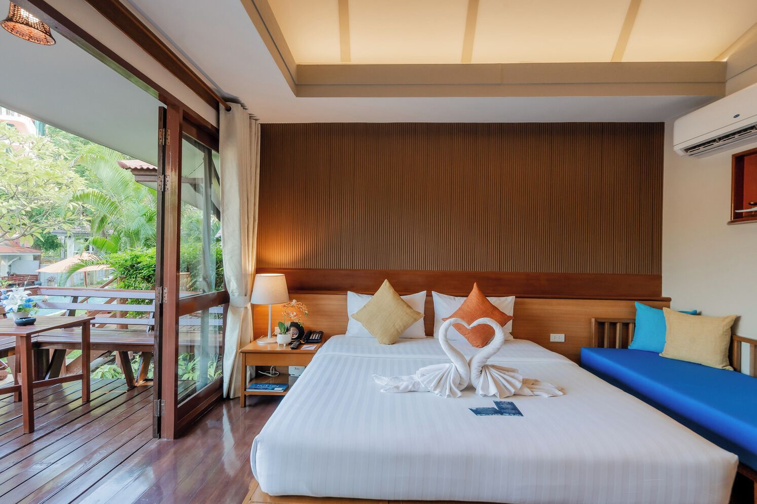 A hotel room with a large bed, wooden headboard, and a view of a pool and greenery outside.