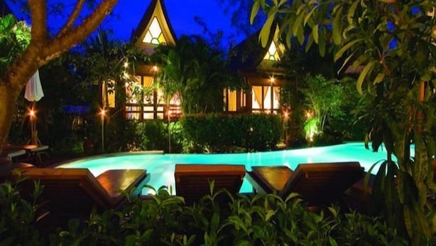 A resort with a swimming pool, lounge chairs, and a building with a distinctive roof. - Baan Duangkaew (Hua Hin)