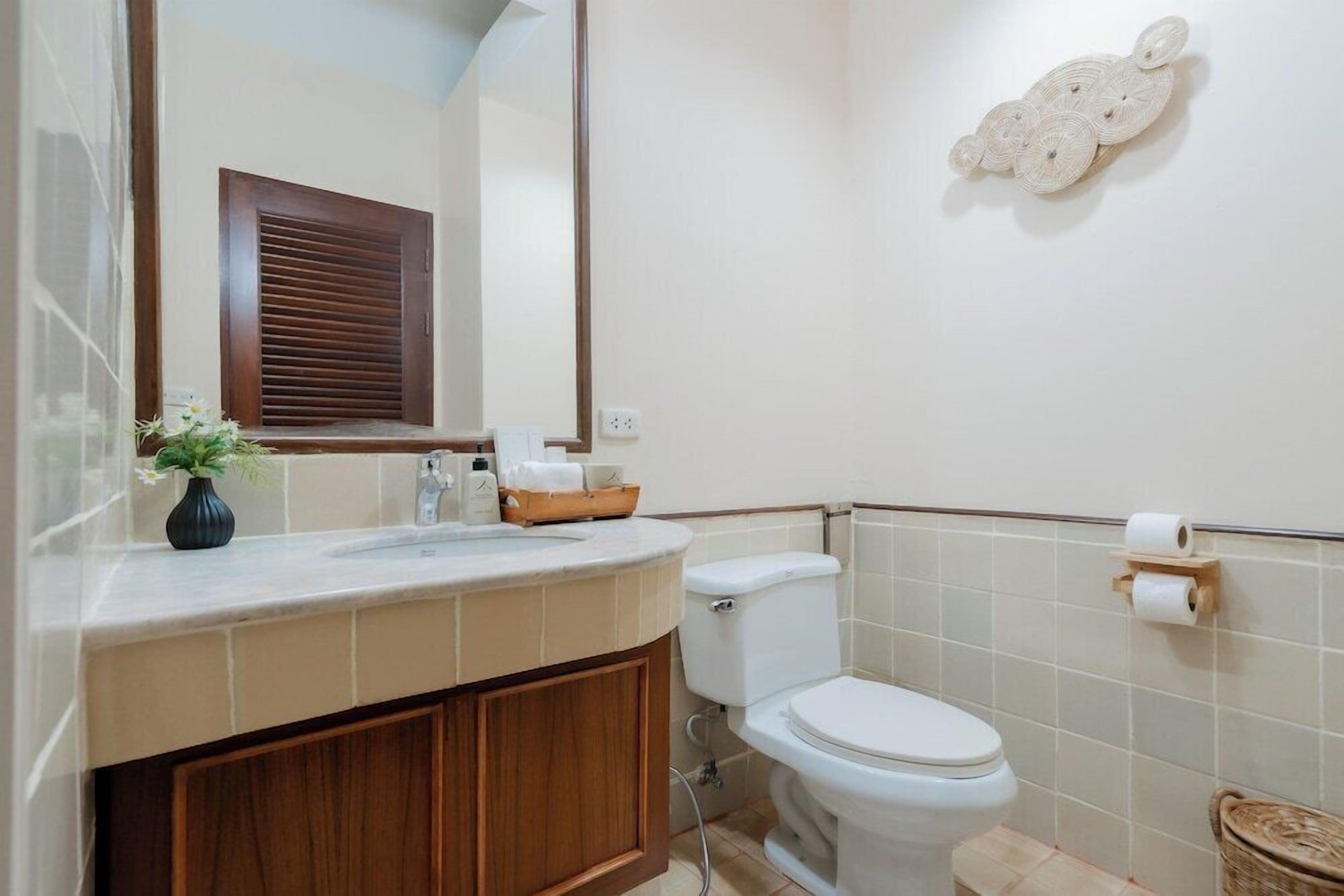 A bathroom with a toilet, sink, and mirror. There is a vase with flowers on the sink counter.